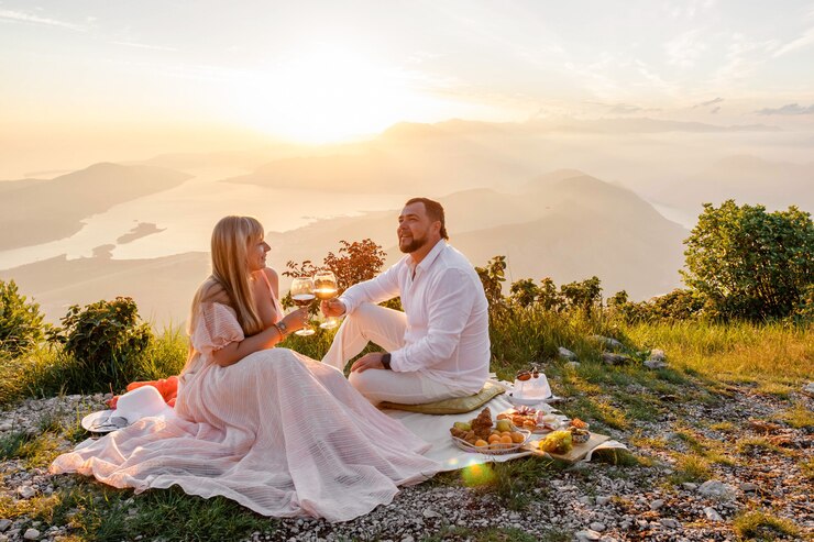 Giovane coppia con un picnic al tramonto in montagna, felice, ridendo