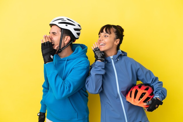 Giovane coppia di ciclisti isolata su sfondo giallo che grida con la bocca spalancata lateralmente