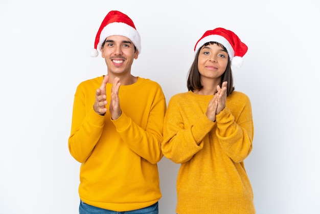 Giovane coppia di razza mista che celebra il Natale isolato su sfondo bianco che applaude dopo la presentazione in una conferenza