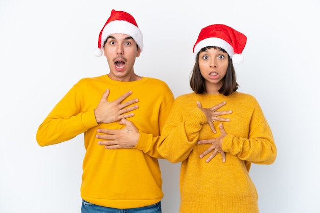 Giovane coppia di razza mista che celebra il Natale isolato su sfondo bianco sorpreso e scioccato mentre guarda a destra