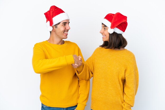 Giovane coppia di razza mista che celebra il Natale isolato su sfondo bianco, stretta di mano dopo un buon affare