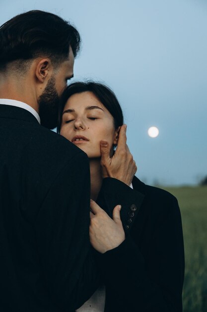 Giovane coppia elegante di marito e moglie vestita con abiti classici durante un servizio fotografico in mezzo a un campo verde Il concetto di relazione tra una coppia di persone innamorate