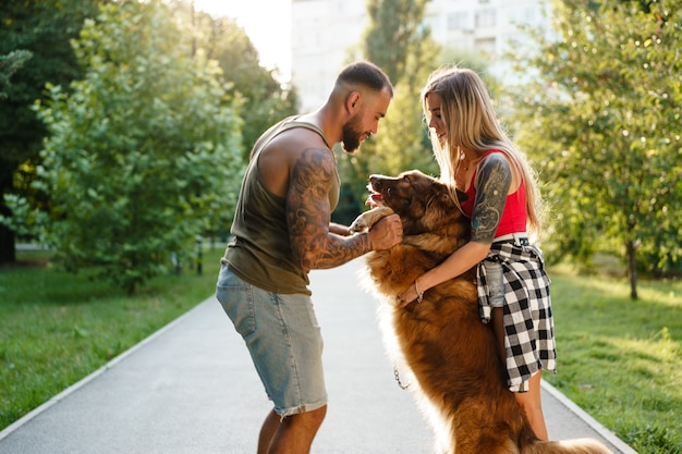 Giovane coppia felice che gioca con il loro cane sorridente nel parco