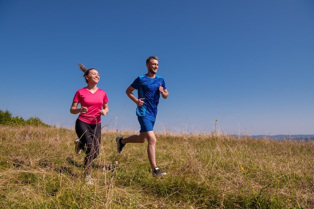 giovane coppia felice che gode di uno stile di vita sano mentre fa jogging su un prato in una bella montagna estiva soleggiata, esercizio fisico e concetto di fitness