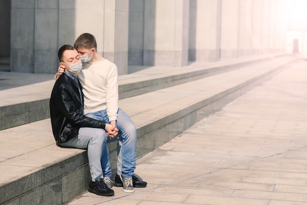 Giovane coppia gay che indossa una maschera medica, si abbraccia e si bacia in città.