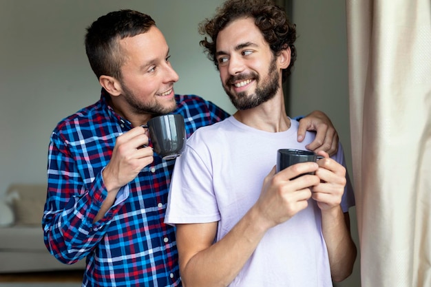 Giovane coppia gay innamorata che guarda fuori dalla finestra Due giovani uomini androgini che sorridono insieme e bevono caffè