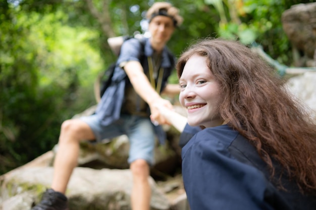 Giovane coppia in escursione nella foresta si aiutano a vicenda nell'arrampicata uomo e donna in trekking in natura