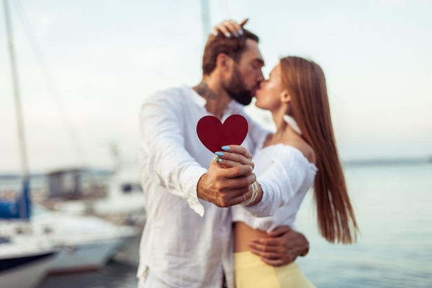 Giovane coppia innamorata che si bacia con un cuore rosso che mostra il loro amore in un yacht club concetto d'amore romantico