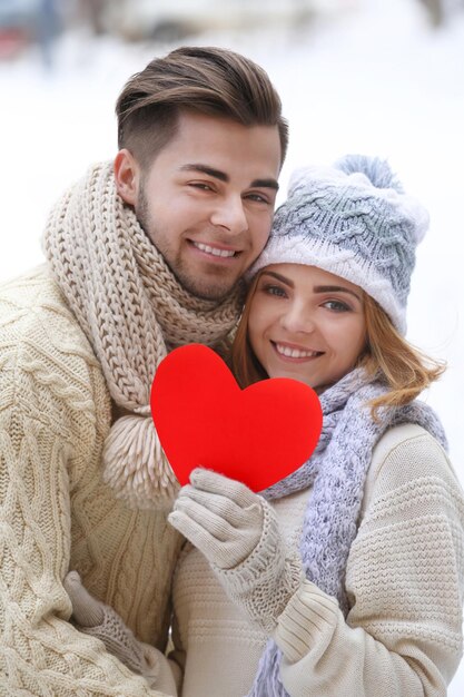 Giovane coppia innamorata che tiene cuore di carta rossa all'aperto in inverno