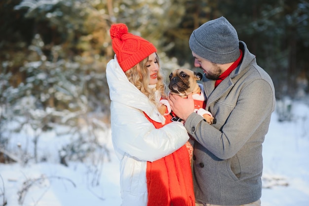 Giovane coppia innamorata del cane che cammina nel bosco innevato.