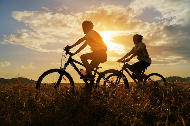 Giovane coppia innamorata divertente e felice in mountain bike dopo l'epidemia di coronavirus covid-19. Fine dell'epidemia di coronavirus. Silhouette ciclismo uomo e donna in mountain bike all'ora del tramonto.