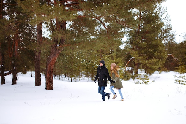 Giovane coppia innamorata in esecuzione e mano nella mano nella foresta di inverno nevoso
