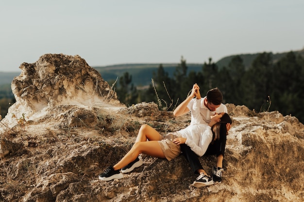 Giovane coppia innamorata seduta su una pietra che si affaccia e si guarda l'un l'altro le montagne
