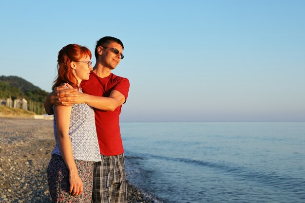 Giovane coppia innamorata sta in riva al mare e guarda il tramonto