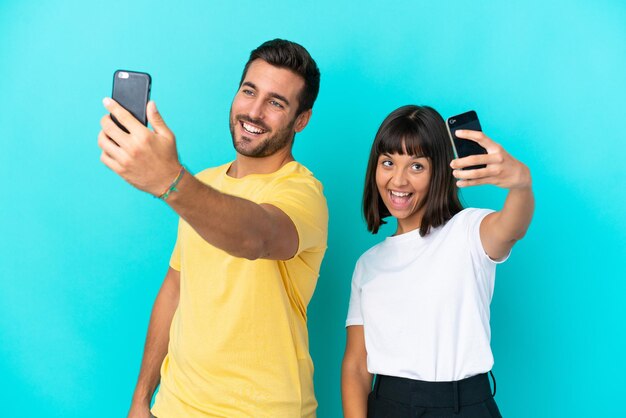 Giovane coppia isolata su sfondo blu che fa un selfie con il cellulare