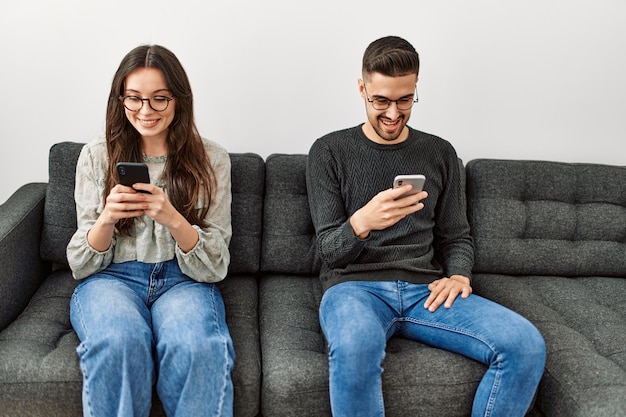 Giovane coppia ispanica che usa lo smartphone seduta sul divano a casa