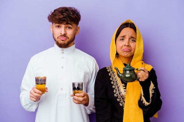Giovane coppia marocchina bere il tè per celebrare il mese del ramadan isolato su sfondo viola