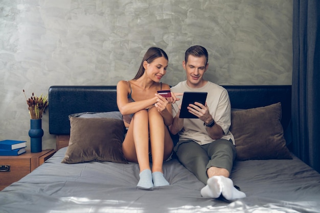 Giovane coppia seduta nella camera da letto usando l'app di pagamento online Unveiling