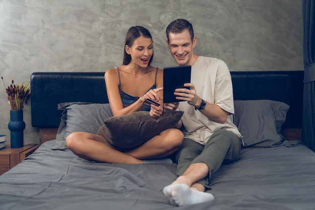 Giovane coppia seduta nella camera da letto usando l'app di pagamento online Unveiling