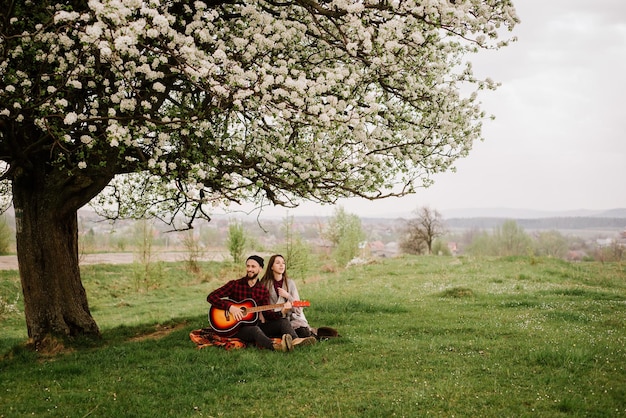 Giovane coppia seduta sotto il grande albero e l'uomo che suona la chitarra