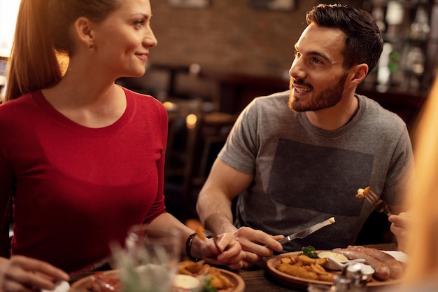 Giovane coppia sorridente mangiare in un pub e parlare tra loro Focus è sull'uomo