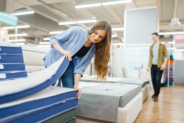 Giovane coppia sorridente nello showroom del negozio di mobili. Uomo e donna in cerca di campioni per la camera da letto in negozio, marito e moglie acquistano beni per interni domestici moderni