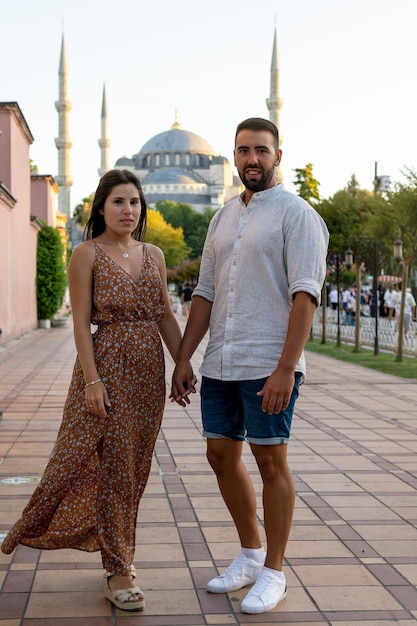 Giovane coppia sposata che si tiene per mano e posa con la Moschea Blu sullo sfondo al tramonto