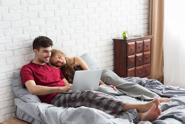 Giovane coppia sposata sdraiata sul letto e usando il laptop a casa