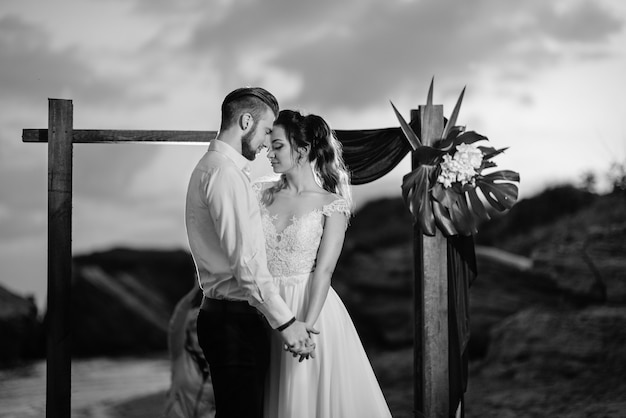 Giovane coppia sposo e sposa con un bouquet la sera sulla spiaggia vicino all'arco nuziale