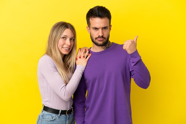 Giovane coppia su sfondo giallo isolato frustrata e puntando il dito di lato