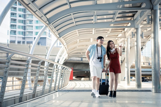 Giovane coppia trascinando una valigia e parlando allegramente sorridendo mentre si viaggia in città. La felicità del giovane e della giovane donna in viaggio viaggiano insieme. concetto di viaggio.