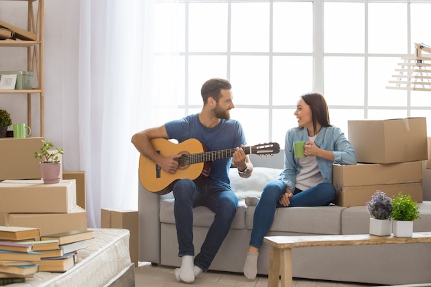 Giovane coppia uomo e donna che si trasferiscono insieme in un nuovo appartamento a suonare la chitarra