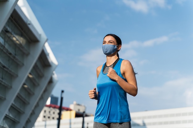 Giovane corridore caucasica dai capelli scuri in maschera protettiva che fa jogging nel centro della città