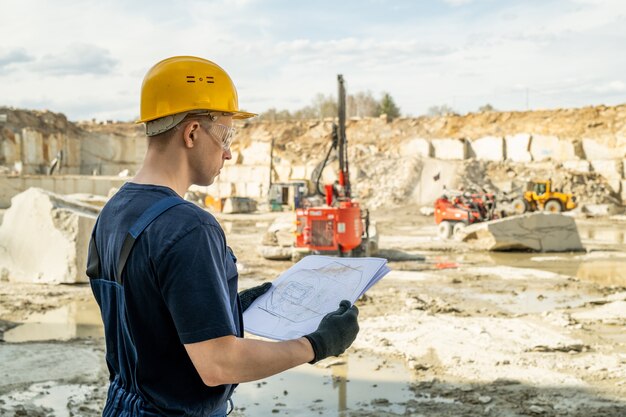 Giovane costruttore in abiti da lavoro che tiene schizzo di costruzione