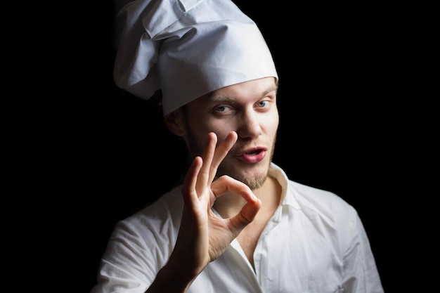 giovane cuoco maschio in uniforme bianca su sfondo scuro in cucina
