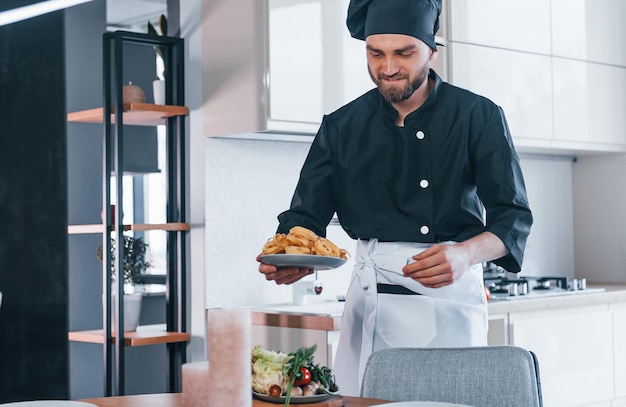 Giovane cuoco professionista in uniforme che fa insalata in cucina