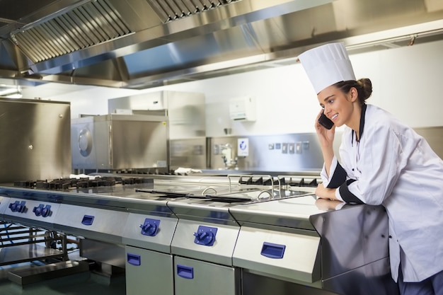 Giovane cuoco unico felice che sta accanto alla superficie di lavoro che telefona