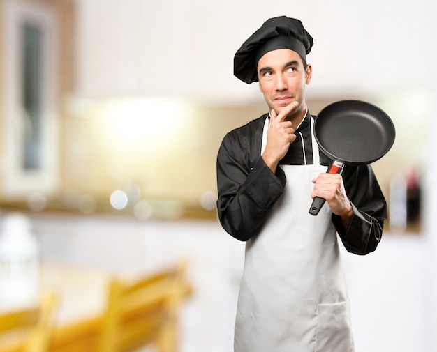 Giovane cuoco utilizzando un utensile da cucina con un gesto di dubbio