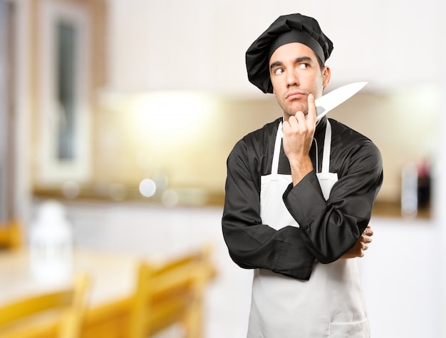 Giovane cuoco utilizzando un utensile da cucina con un gesto di dubbio