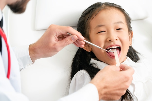 Giovane dentista amichevole che esamina i denti di bambino felice in clinica dentale. Concetto di odontoiatria.