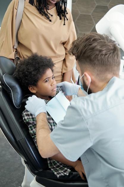 Giovane dentista che mette il tovagliolo sul petto del piccolo paziente