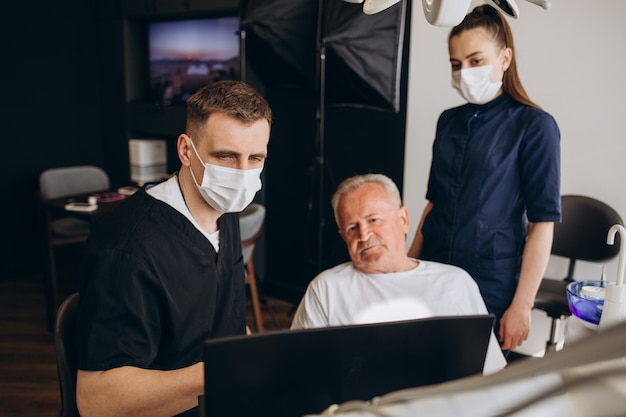 Giovane dentista e il suo assistente che curano l'uomo anziano