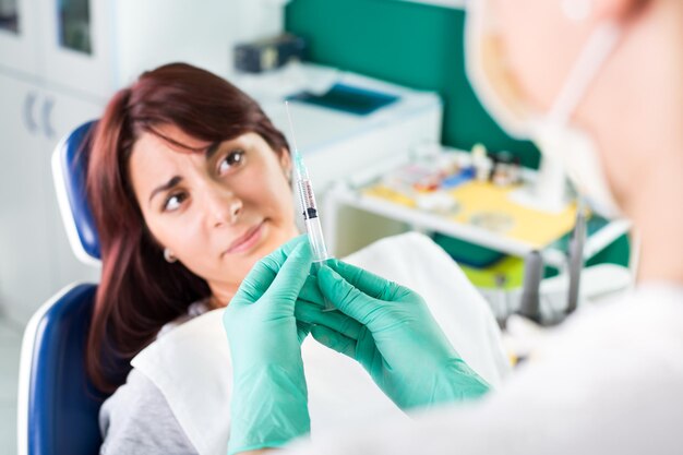 Giovane dentista femminile che dà anestesia al paziente prima della chirurgia dentale. Il paziente nella paura che esprime negatività. Focus selettivo, focus sul paziente.