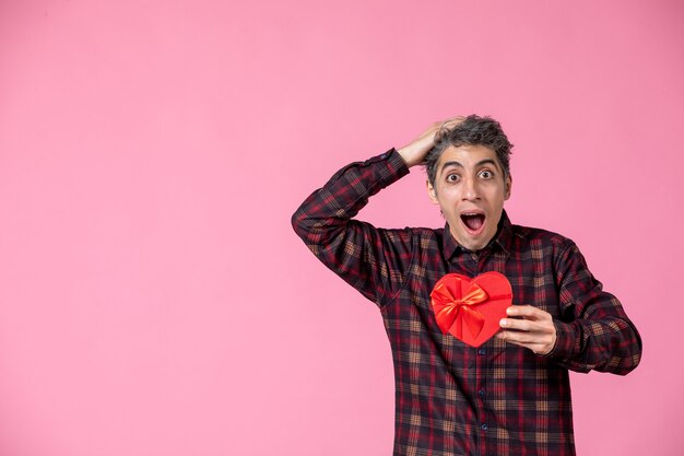 Giovane di vista frontale che tiene presente a forma di cuore rosso sulla parete rosa