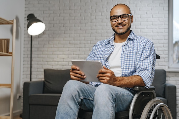 Giovane disabile afroamericano seduto su una sedia a rotelle e usa un tablet digitale