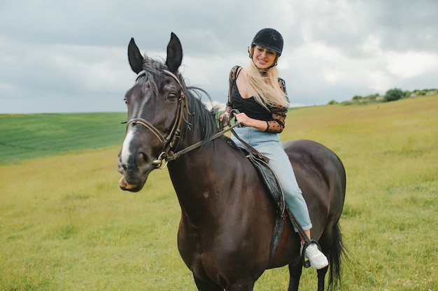 Giovane donna a cavallo sul campo verde