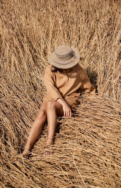 Giovane donna a piedi nudi in abiti di lino e un cappello su uno sfondo di erba secca ragazza romantica con un cappello