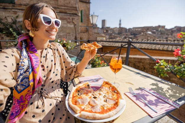 Giovane donna a pranzo con pizza e vino al ristorante all'aperto nella città di Siena