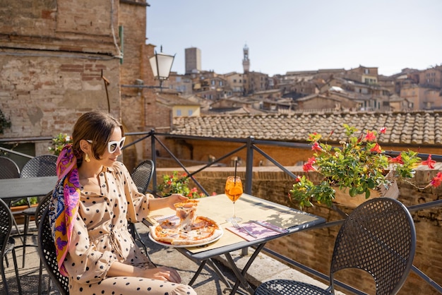 Giovane donna a pranzo con pizza e vino al ristorante all'aperto nella città di Siena
