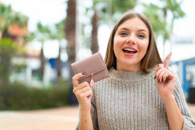 Giovane donna abbastanza bionda che tiene un portafoglio all'aperto che indica una grande idea